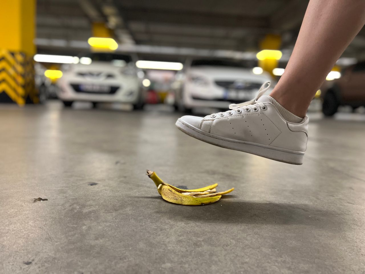 who-we-are Close-up of a foot about to step on a banana peel in an underground parking lot.