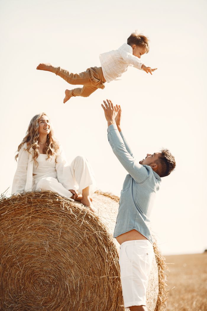 why-choose-us Joyful family moment catching son mid-air on hay bale in countryside.