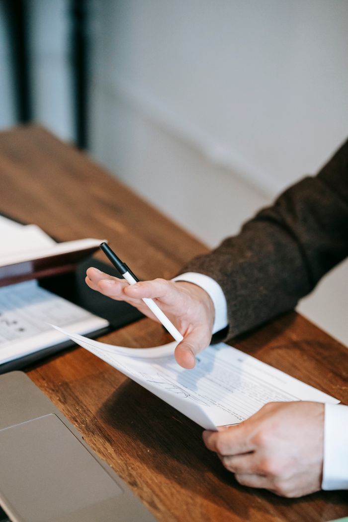 who-we-are Close-up of a businessman in a suit analyzing papers on a wooden desk.