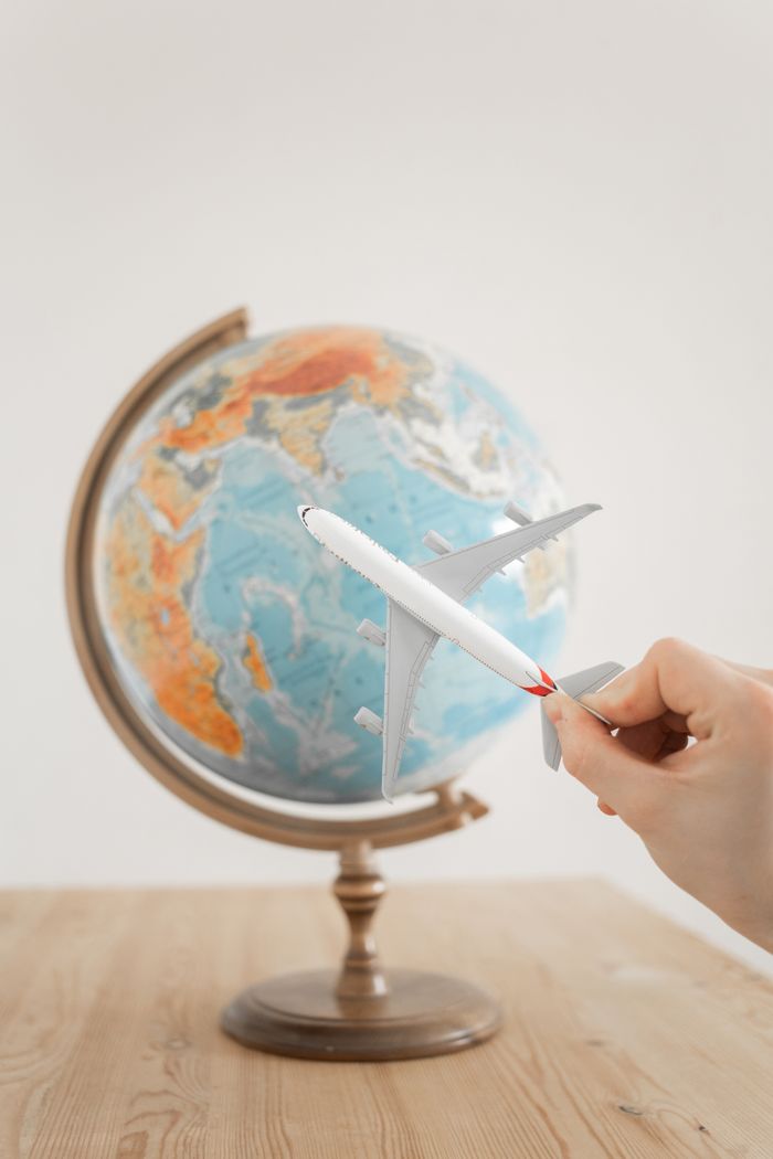 team-02 Close-up of a hand with a toy airplane in front of a globe, symbolizing travel and exploration.